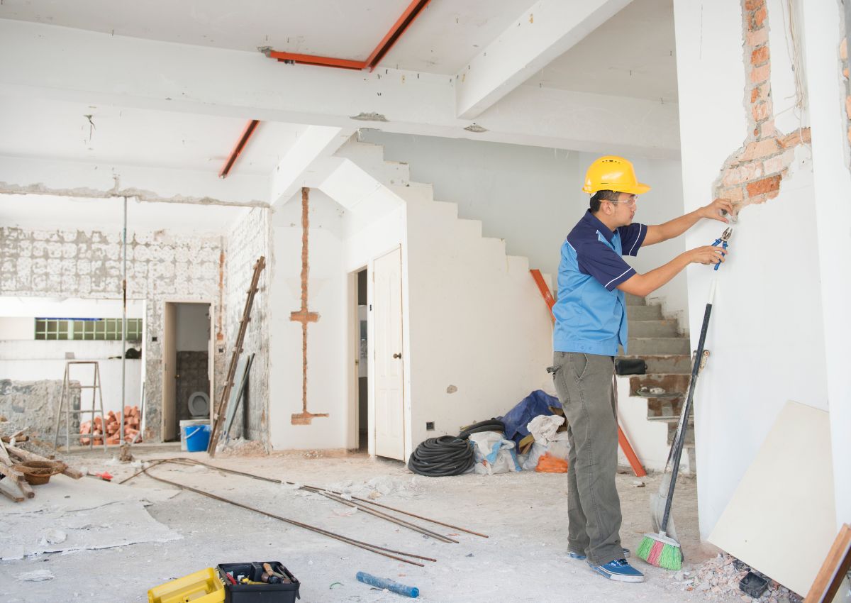 Ouvrier en bâtiment avec casque de sécurité travaillant sur un mur pendant une rénovation maison.