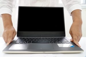 Personne tenant un ordinateur portable noir à écran éteint, idéal pour remplacer un ordinateur lent