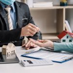 Agent d'une agence immobilière transmettant les clés d'un bien sur un bureau avec maquettes de maisons