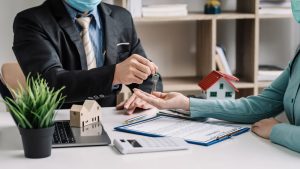 Agent d'une agence immobilière transmettant les clés d'un bien sur un bureau avec maquettes de maisons