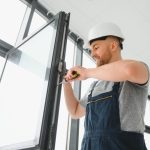 Artisan menuisier effectuant les derniers réglages lors de la pose fenêtres en aluminium noir dans un bâtiment moderne