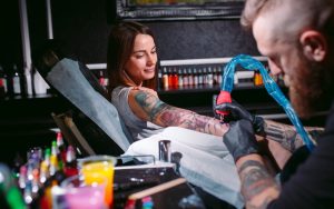 Une cliente souriante reçoit un tatouage coloré sur le bras de la part d'un artiste barbu dans un salon de tatouage professionnel et moderne