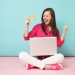 Une femme joyeuse avec un ordinateur portable et une carte cadeau, illustrant comment l'e-coupon est l'atout idéal pour accroître le volume des ventes.
