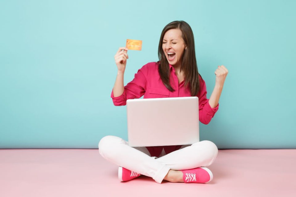 Une femme joyeuse avec un ordinateur portable et une carte cadeau, illustrant comment l'e-coupon est l'atout idéal pour accroître le volume des ventes.